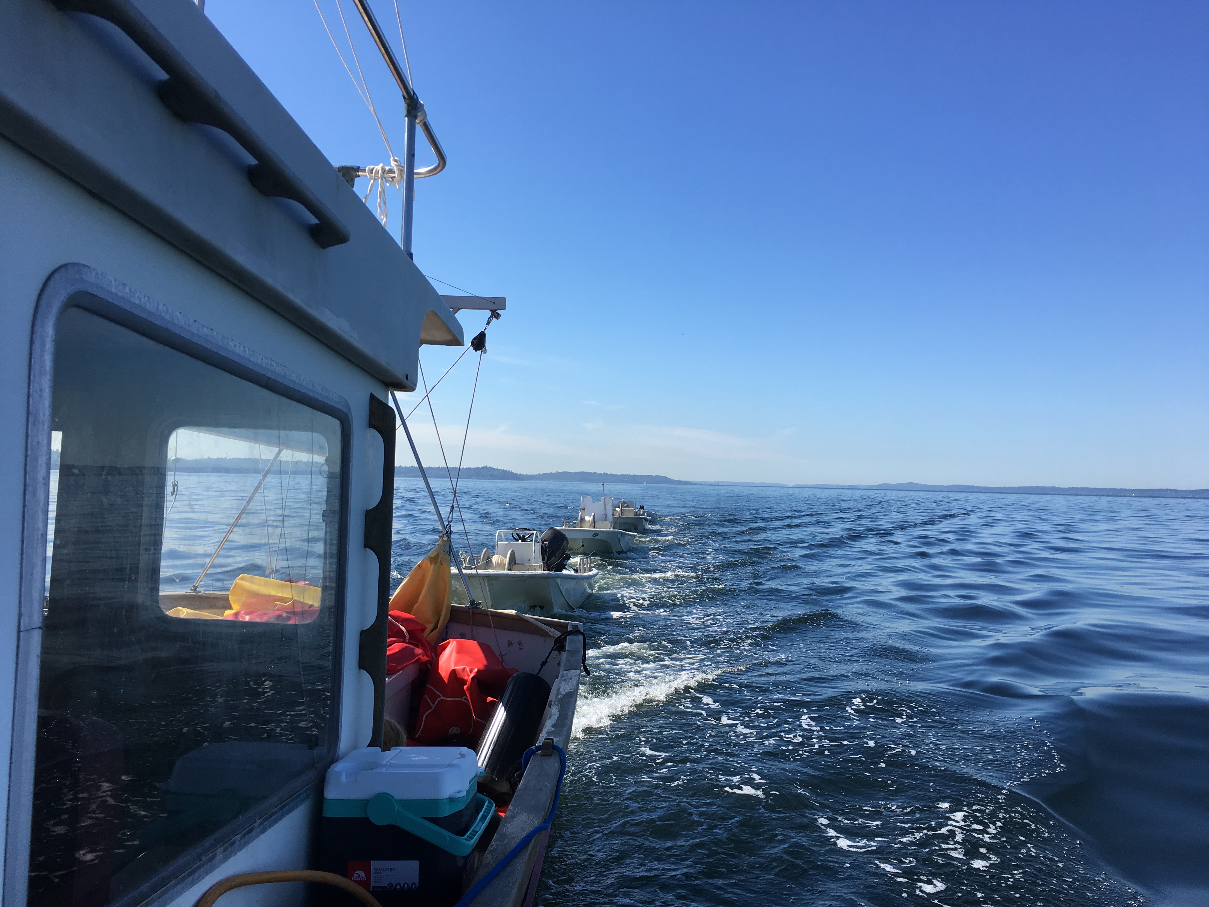 Boat underway with support craft in tow on a bright day.