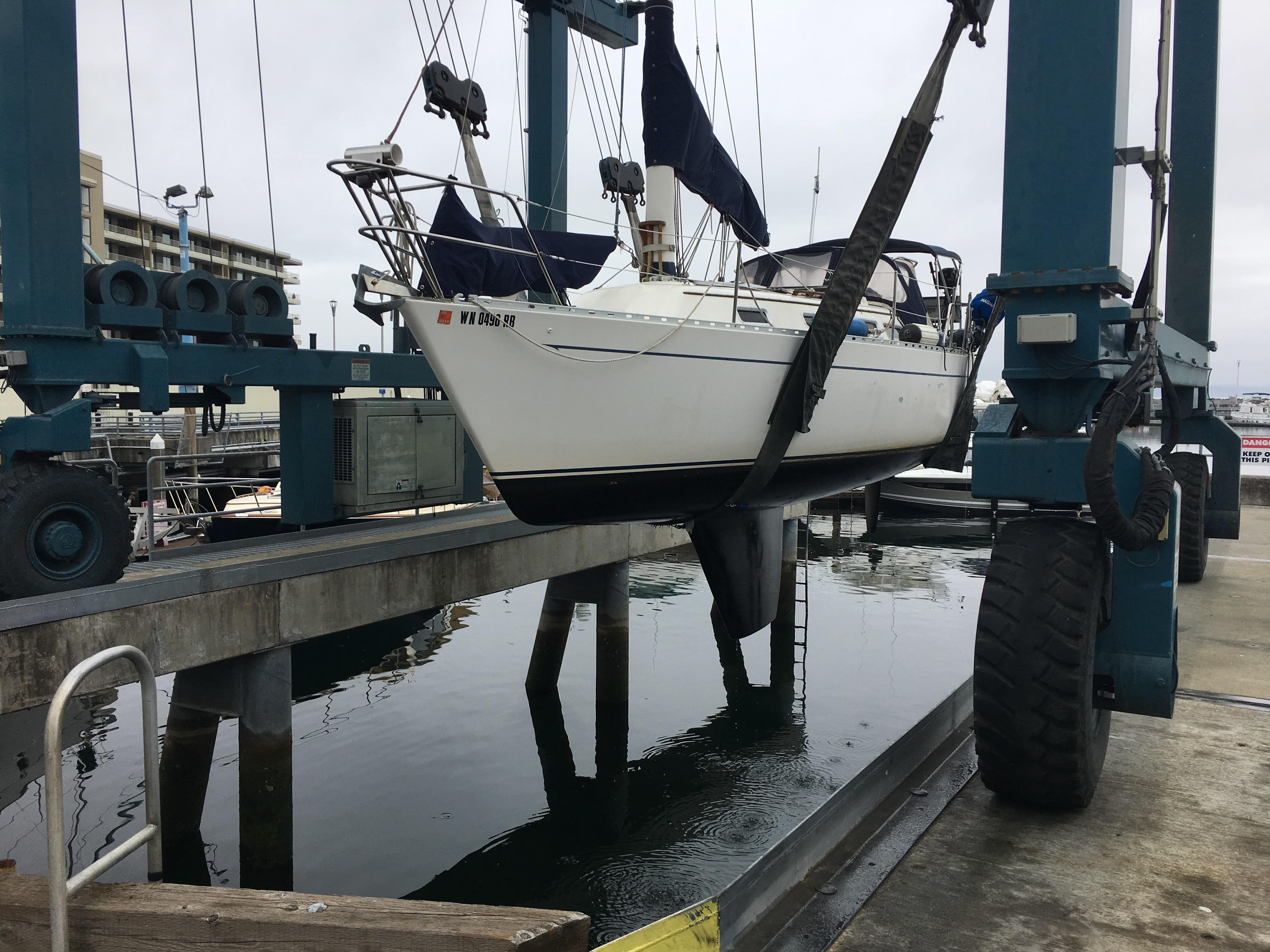 Sailboat lifted in a marina haulout sling for maintenance.