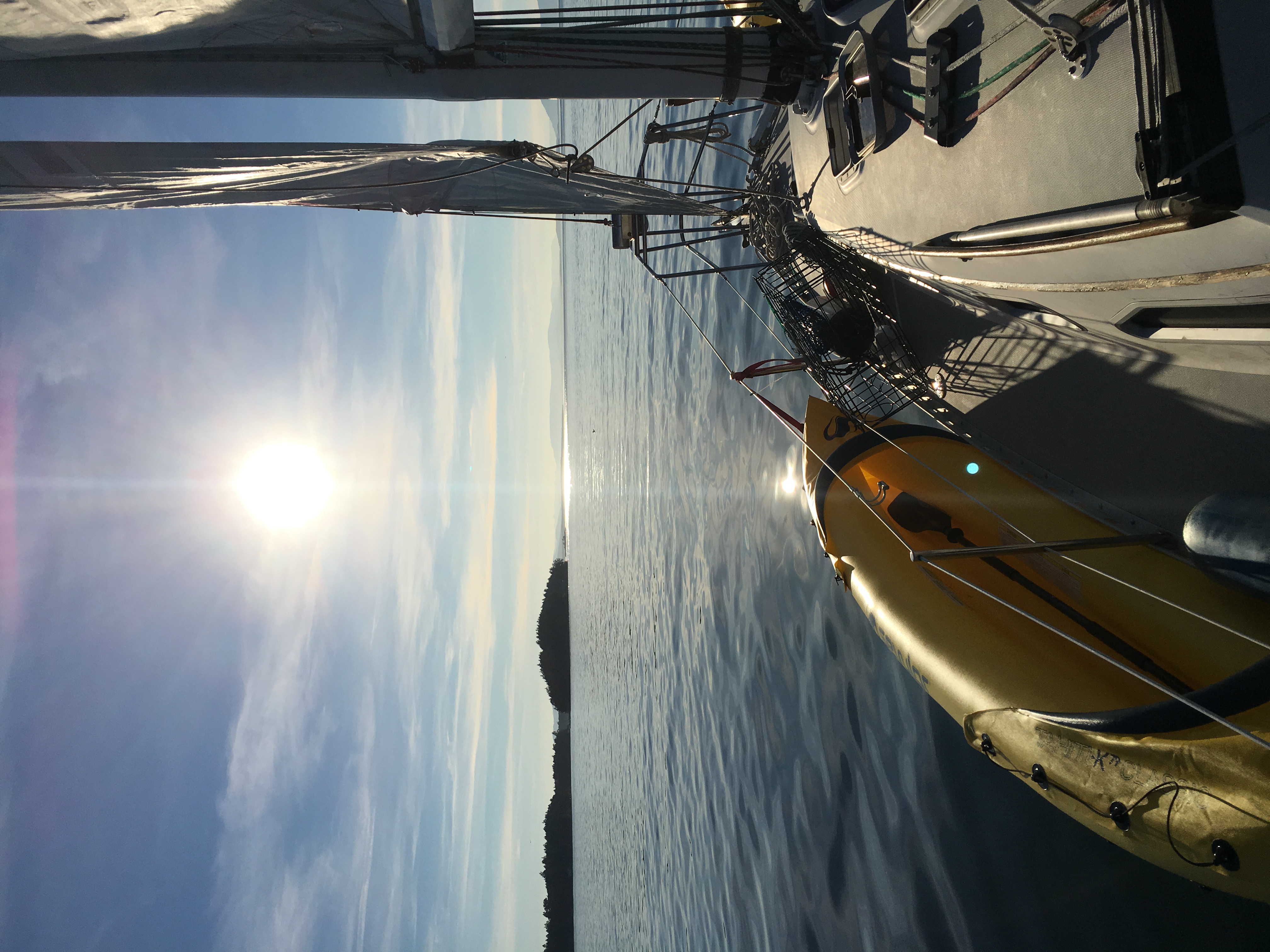 Bright sky and smooth water seen from the deck of a sailboat.